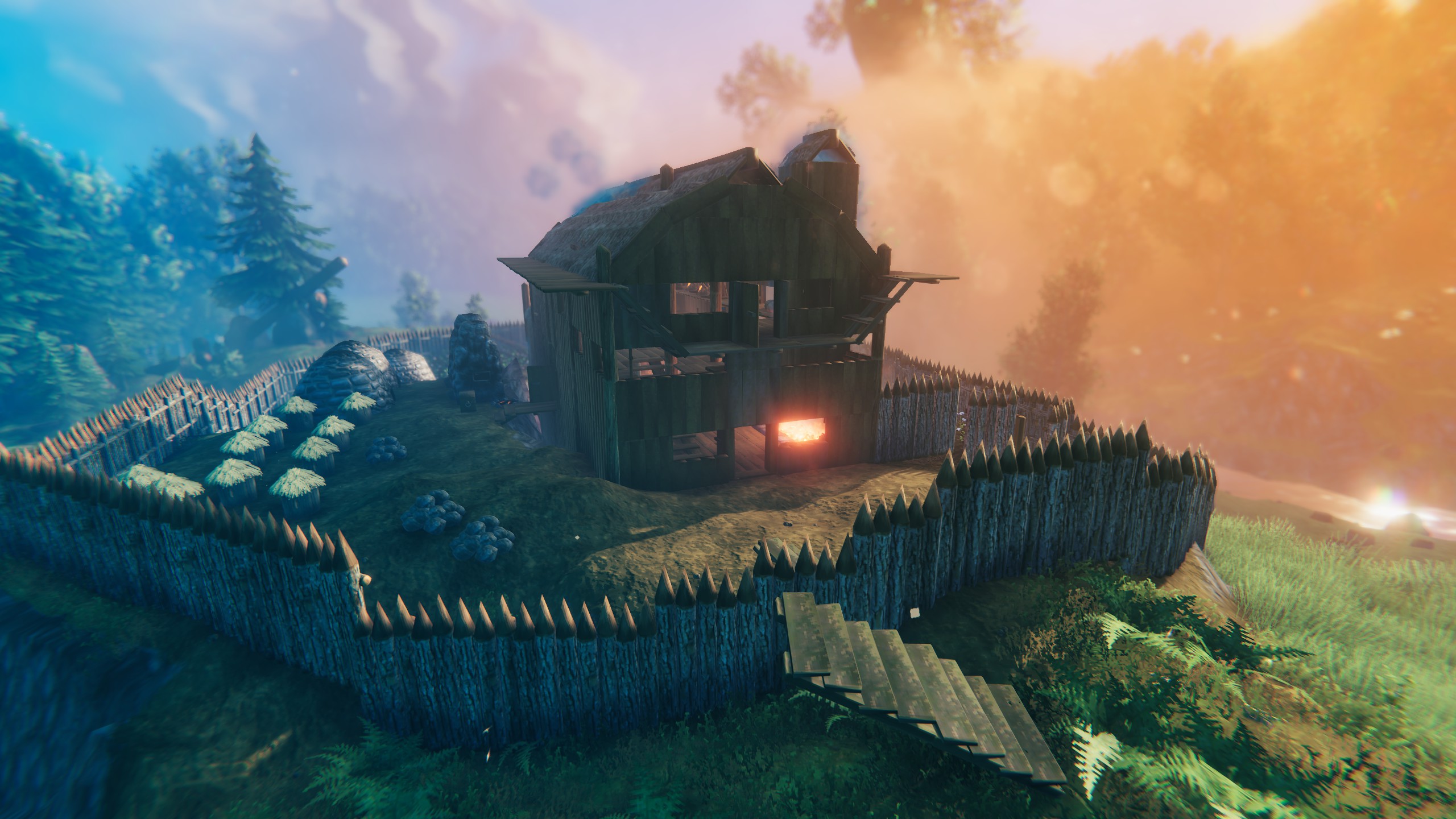 A hilltop base ringed by a sharpened palisade, with crop rows and an open hearth, lit by sunrise.
